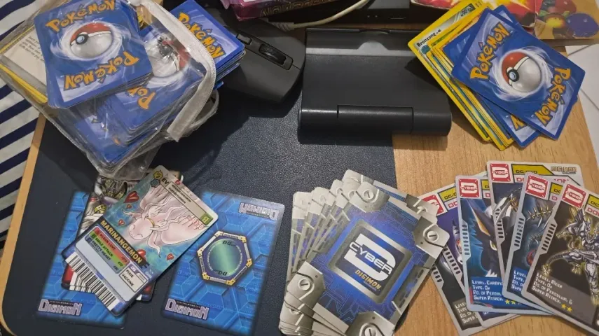 A desk covered in piles of Pokemon cards, older Digimon cards and Vanguard cards.