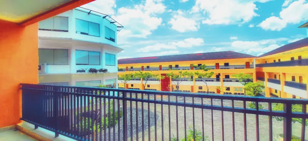 Colour-graded photo looking along a balcony railing at a yellow, orange and blue low-rise building under a bright sky.